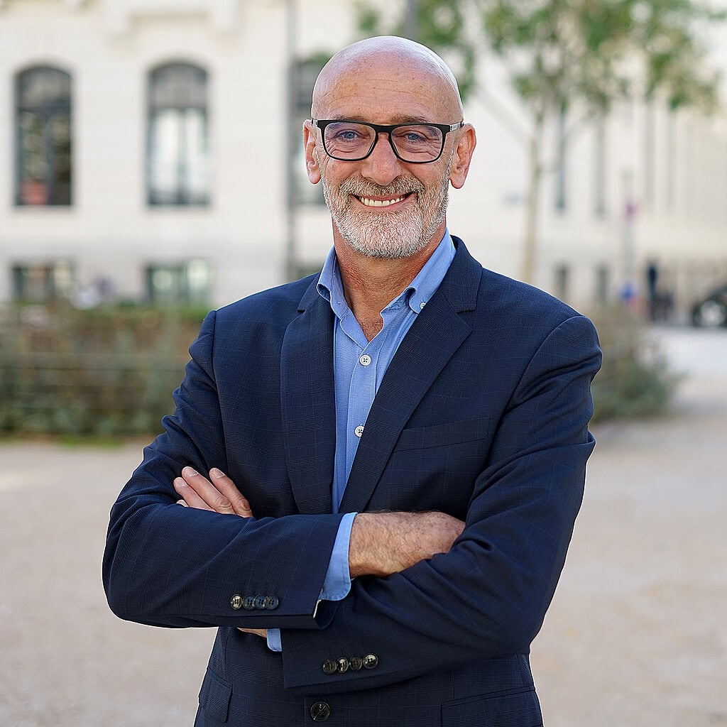 Portrait professionnel à Lyon en extérieur. Dirigeant souriant en costume bleu, bras croisés. Photographe portrait professionnel Lyon spécialisé en portraits corporate.